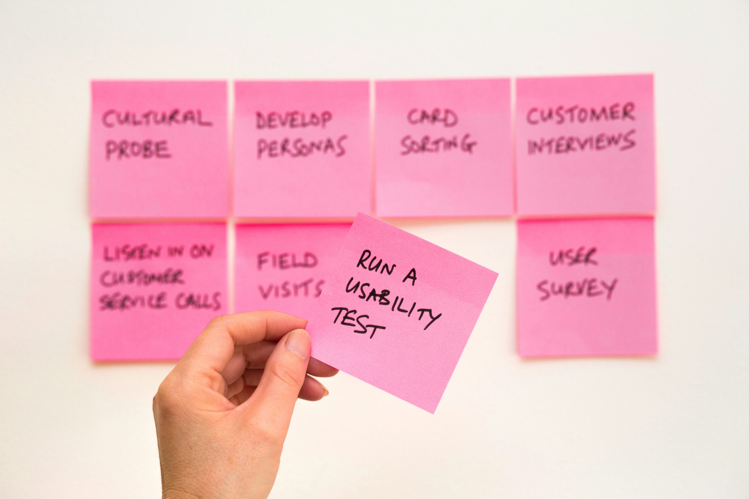 A person holding a pink sticky-note, which states ‘Run a usability test’