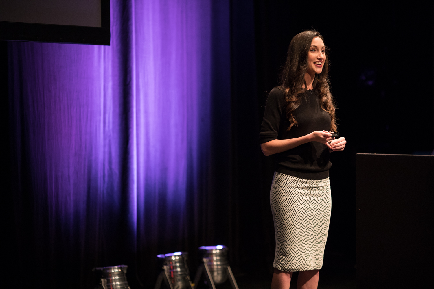 Molly Nix is on the stage of UX London in 2019, speaking there for the first time. The stage is dark/black, with a violet color highlight behind the speaker